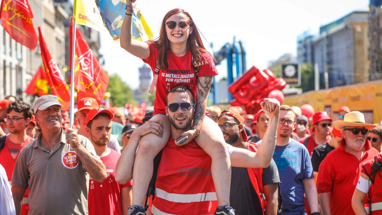Junge Frau sitzt auf der FairWandel-Kundgebung am 29. Juni 2019 auf den Schultern von einem jungen Mann. Beide heben kämpferisch die Faust nach oben.