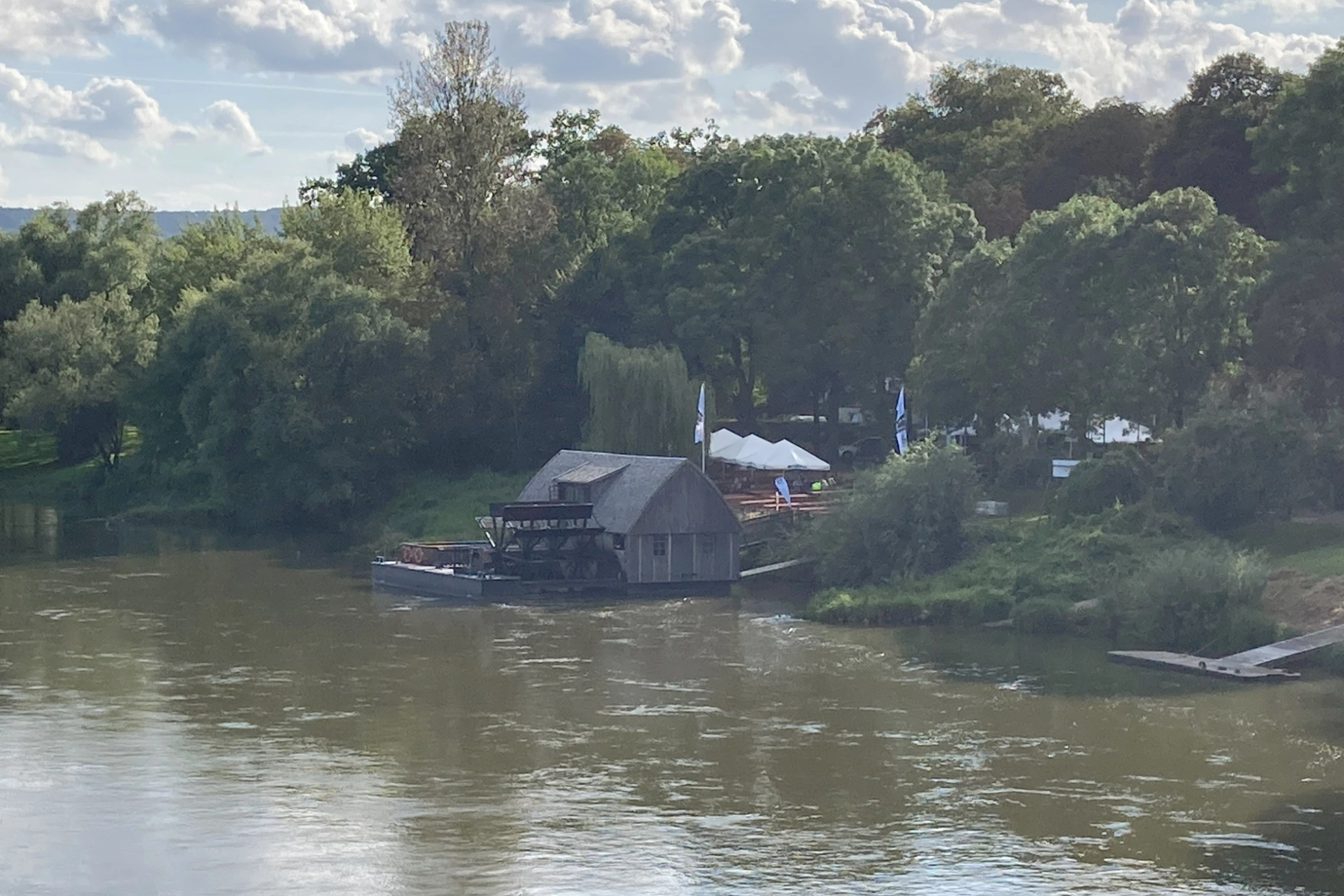 Im Vordergrund ist die Weser zu sehen. Im Hintergrund ist die Mindener Schiffsmühle zu sehen. Ein beliebtes Mindener Ausflugslokal an der Weserpromenade. Weiße Schirme laden zum Verweilen ein.